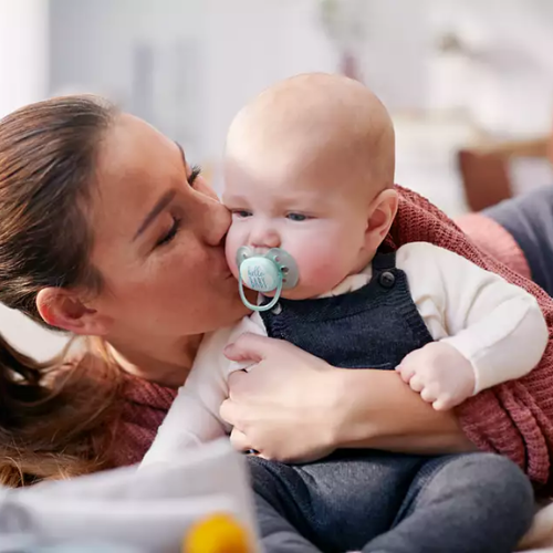 madre besando a su bebé en la mejilla mientras el bebé tiene un chupete philips avent